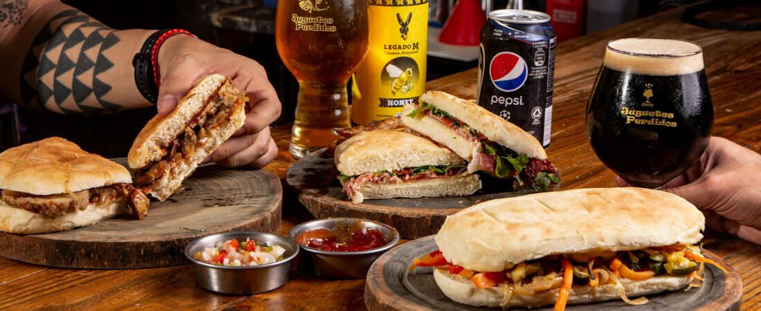 Close-up of gourmet sandwiches paired with craft beers on a rustic wooden table.