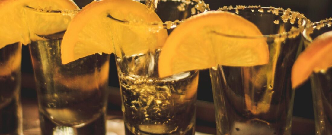 Bartender pouring alcohol into shot glasses garnished with lemon slices, perfect for nightlife imagery.