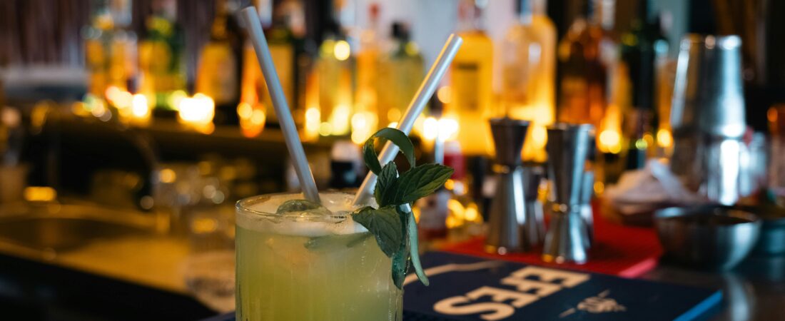 A vibrant, minty cocktail with straws, set against a backdrop of a dimly lit bar.